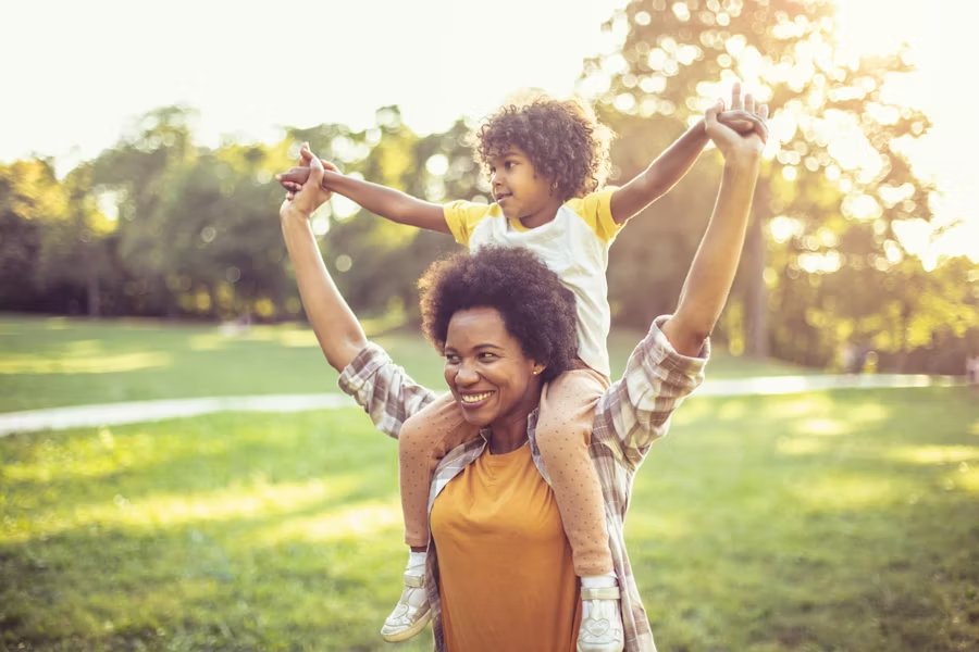 Mom and daughter laughing together outside, warm and genuine at a table with coffee, looking unhurried